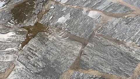 On*: Rain falling on grey stone floor pavement creating ripples and water Stock Footage 345355399
