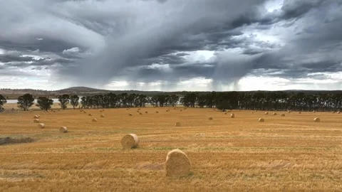 Rain falling from high clouds over hay bales in a dry field Stock Footage 325276658