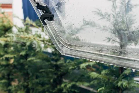 Rain falling over an open window of a caravan Stock Photos