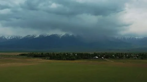 Rain falling over a small village and snowy mountain range Stock Footage 314397668