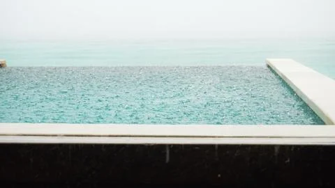 Rain falling on the surface of an infinity pool overlooking the ocean 스톡 사진