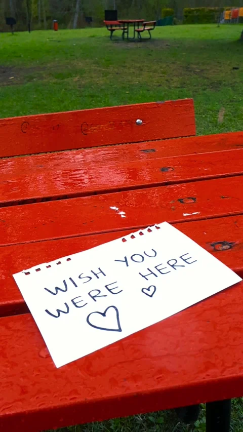Rain Falling on a Wish You Were Here Love Note Left on a Red Picnic Table Stock Footage 335634824