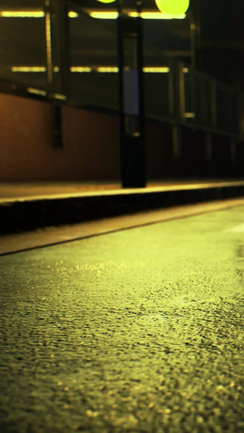 Rain falls on empty street with wet pavement and dim streetlights at night Stock Footage 336579933