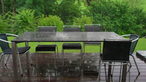Rain falls on modern patio table and chairs in empty backyard, water collecting Stock Footage 313068822