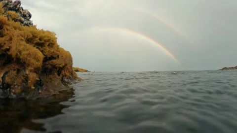 Rain falls on the sea surface with a double rainbow background in the sky Stock Footage 133023299