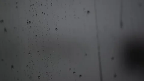 Rain falls on a window, creating drops and streaks during a cloudy day Stock Footage 327990851