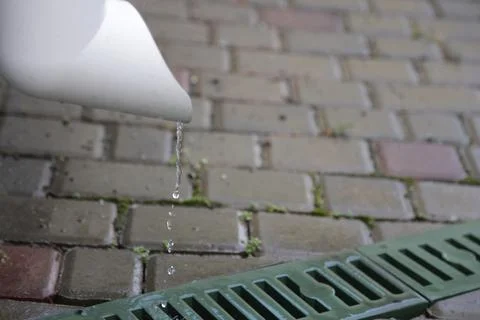 Rain flows down the drain pipe to a green gutter with a grate between the tiles Stock Photos