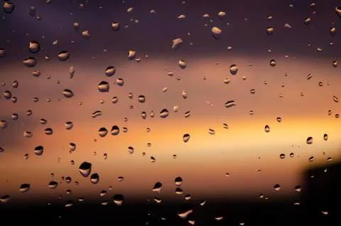 Rain outside window on background of sunset. Rain drops on glass during rain. Stock Photos