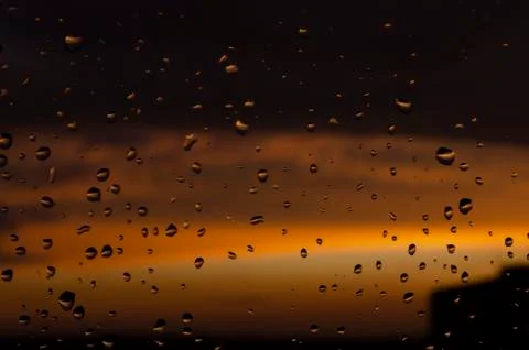 Rain outside window on background of sunset. Rain drops on glass during rain. Stock Photos