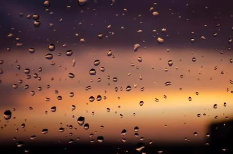 Rain outside window on background of sunset. Rain drops on glass during rain. Stock Photos