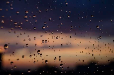 Rain outside window on background of sunset. Rain drops on glass during rain. Stock Photos