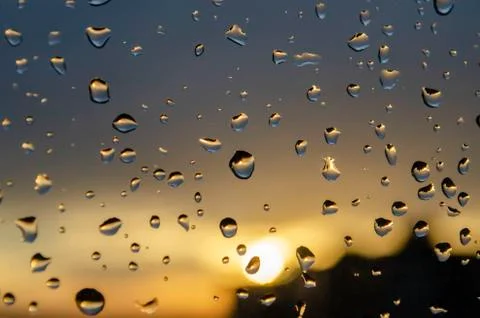 Rain outside window on background of sunset. Rain drops on glass during rain. Stock Photos