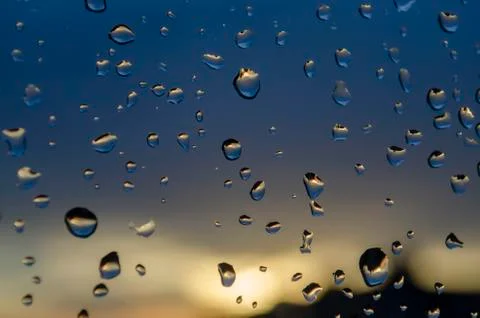 Rain outside window on background of sunset. Rain drops on glass during rain. Stock Photos