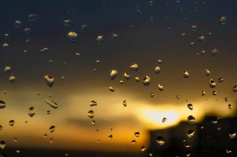 Rain outside window on background of sunset. Rain drops on glass during rain. Stock Photos