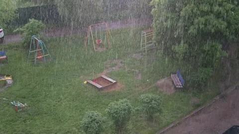 Rain pours down on a playground filled with swings and slides. The area is 库存影片 344450678