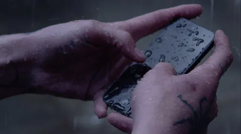 Rain pours down onto a smartphone while hands try to write a txt message. Stock Footage 64863511
