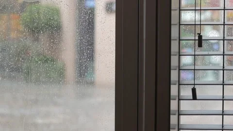 Rain pours outside while blinds filter light through window Stock Footage 303921610