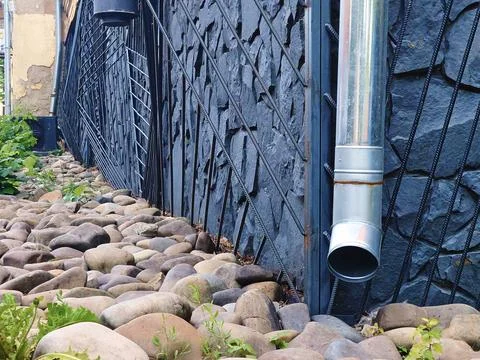 Rain runoff,tin downpipe,decorative cobblestones in yard Stock Photos