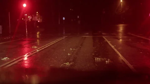 Rain-soaked empty city road at night glowing with red traffic lights and Stock Footage 345530835