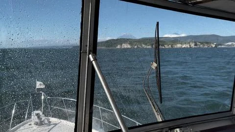 Rain-streaked boat windshield frames a rugged sea passage near Kamchatka 库存照片