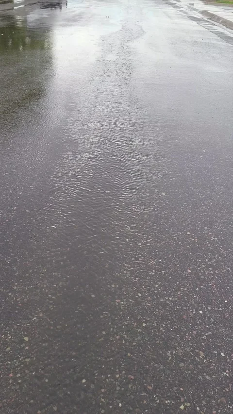 Rain taps asphalt, creating ponding and ripples streaming down road Vidéo 339641316