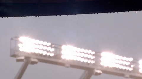 Rain water dripping from ledge and illuminated stadium lights in background Stock Footage 102106838