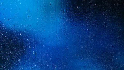 Rain water droplets trickling down the window pane against a blue background Stock Footage 126151793