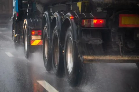Rain water splash flow from wheels of heavy truck moving fast in daylight city 库存照片