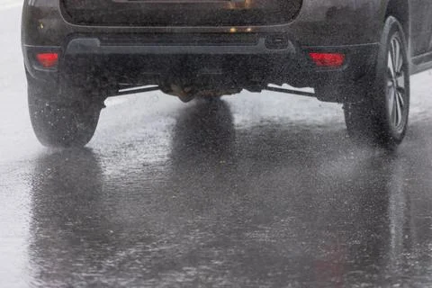 Rain water splash flow from wheels of black car moving fast in daylight city 库存照片