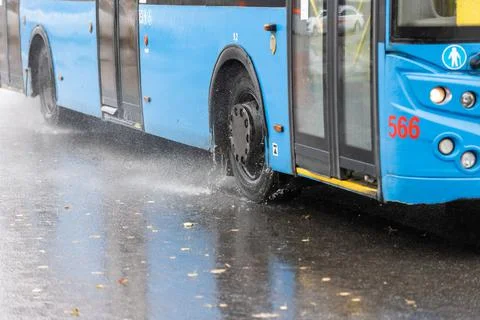 Rain water splashes flow from wheels of blue trolleybus moving in daylight city 库存照片