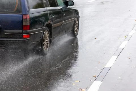 Rain water splashing flows from wheels of old blue car that moving fast on Stock Photos