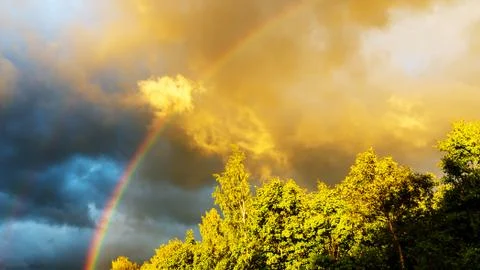 Rainbow after rain in a cloudy sky among dramatic clouds Stock Photos