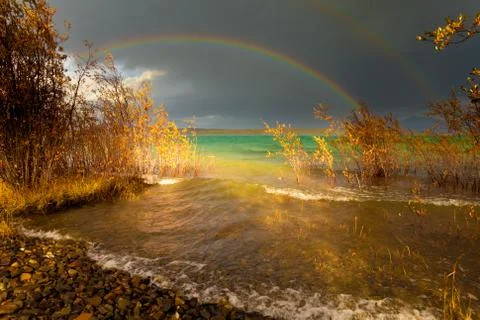 Rainbow and dark clouds over large lake Stock Photos