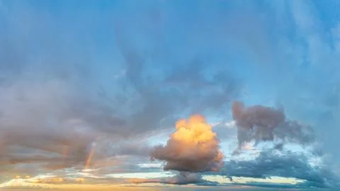 Rainbow and fluffy clouds at sunset after the rain. Stock Photos