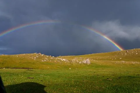 Rainbow appears after storm over grassy hillside 스톡 사진