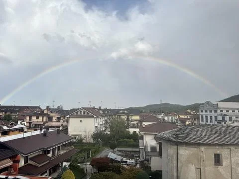Rainbow arch above rooftops and green hills. 스톡 사진