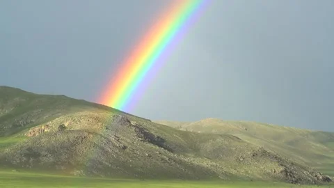 Rainbow arches above a green mountain ridge - Clearing Clouds and Alpine Meadow Stock Footage 339718204