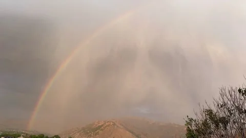 Rainbow arches over mountains as storm clouds disperse, revealing vibrant Stock Footage 344344822