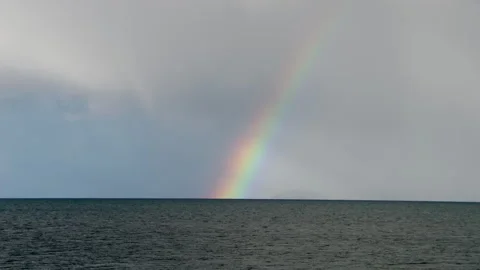 Rainbow Arches Over a Still Lake Beneath Grey Clouds Stock Footage 346504271