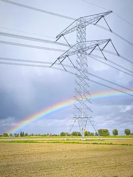 Rainbow arching over high voltage pylon and power lines across rural field Fotos de archivo