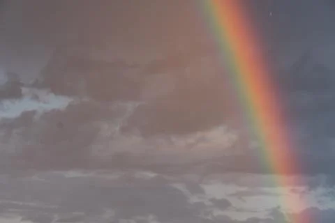 Rainbow arcing across a cloudy sky, contrasting against overcast clouds Vib.. Stock Photos