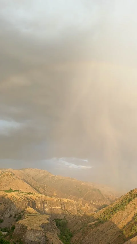 Rainbow arcs over Garni Mountains as sunlight breaks through clouds Stock Footage 344344662