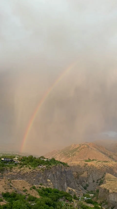 Rainbow arcs over mountainous landscape with clouds and greenery, showcasing a Stock Footage 344723037