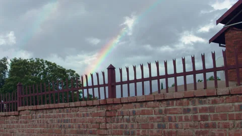 Rainbow in background on cloudy sky with dark tone fence and wall in foreground Stock Footage 229332803