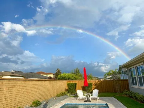 A rainbow in a backyard with a pool Stock Photos