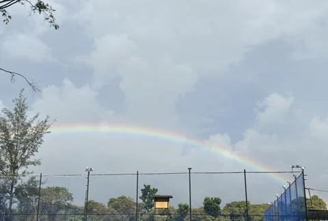Rainbow in a blue sky between tree tops. Bontang, Indonesia Stock Photos