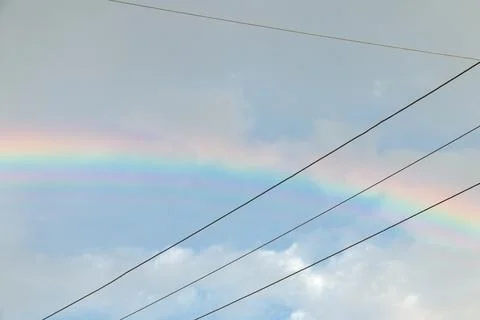 Rainbow bright colors and cables crossed in a sky with clouds Stock Photos