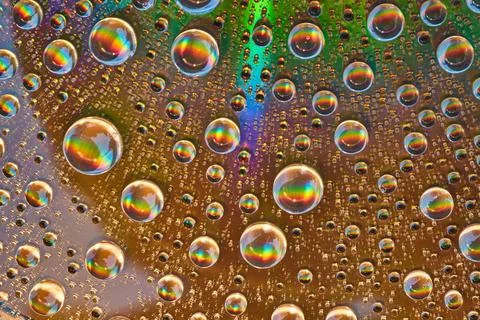 Rainbow bursts inside water drops on reflective metal surface Foto stock
