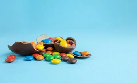 Rainbow candies in broken Chocolate Easter eggs on blue background Stock Photos