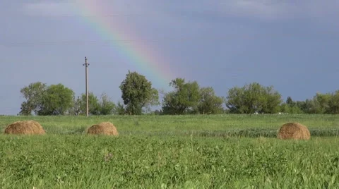 Rainbow in clouded sky over country field with haystacks Video stock 52375348